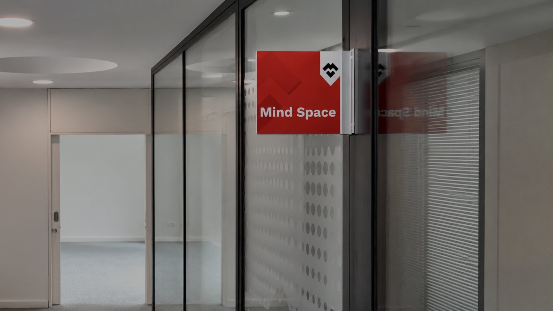 Entrada da sala Mind Space na MaiSpace, com sinalética identificativa e divisórias em vidro.