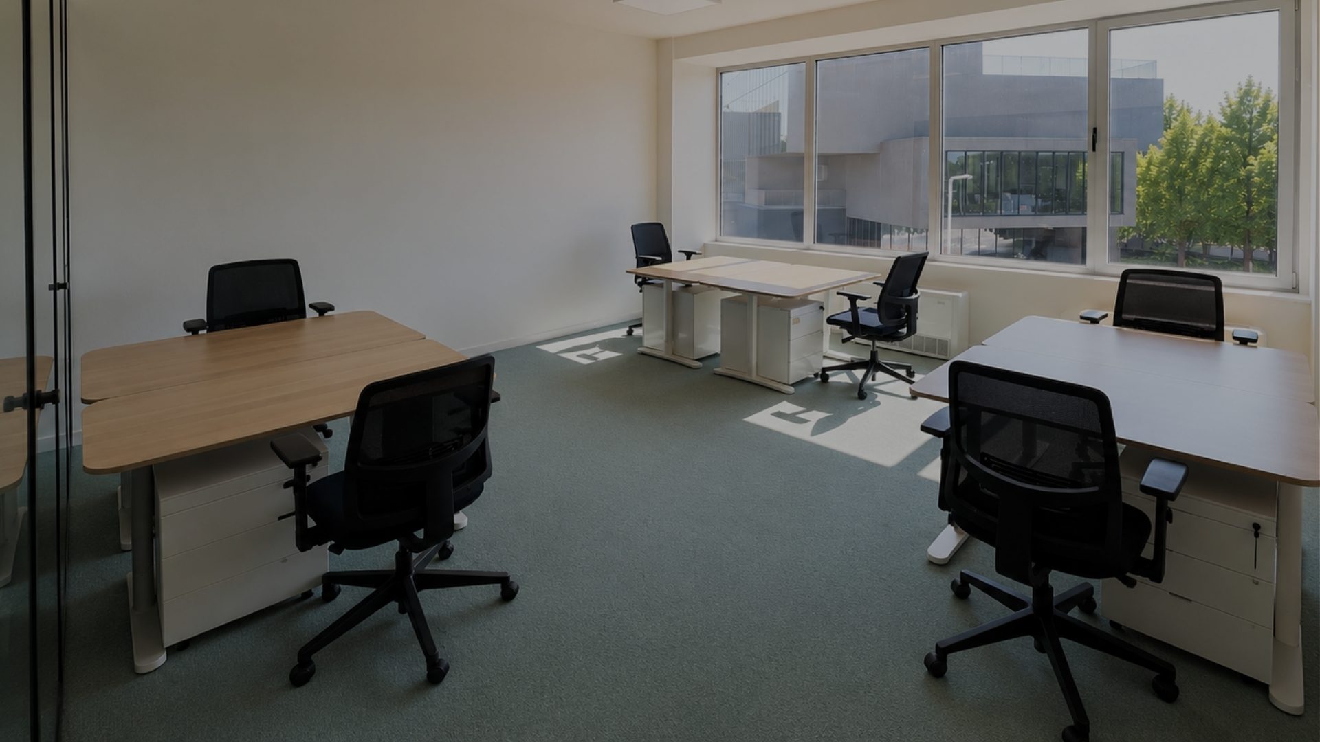 Escritório privado da MaiSpace com secretárias de madeira, cadeiras ergonómicas pretas, janela ampla com luz natural e vista para o exterior.