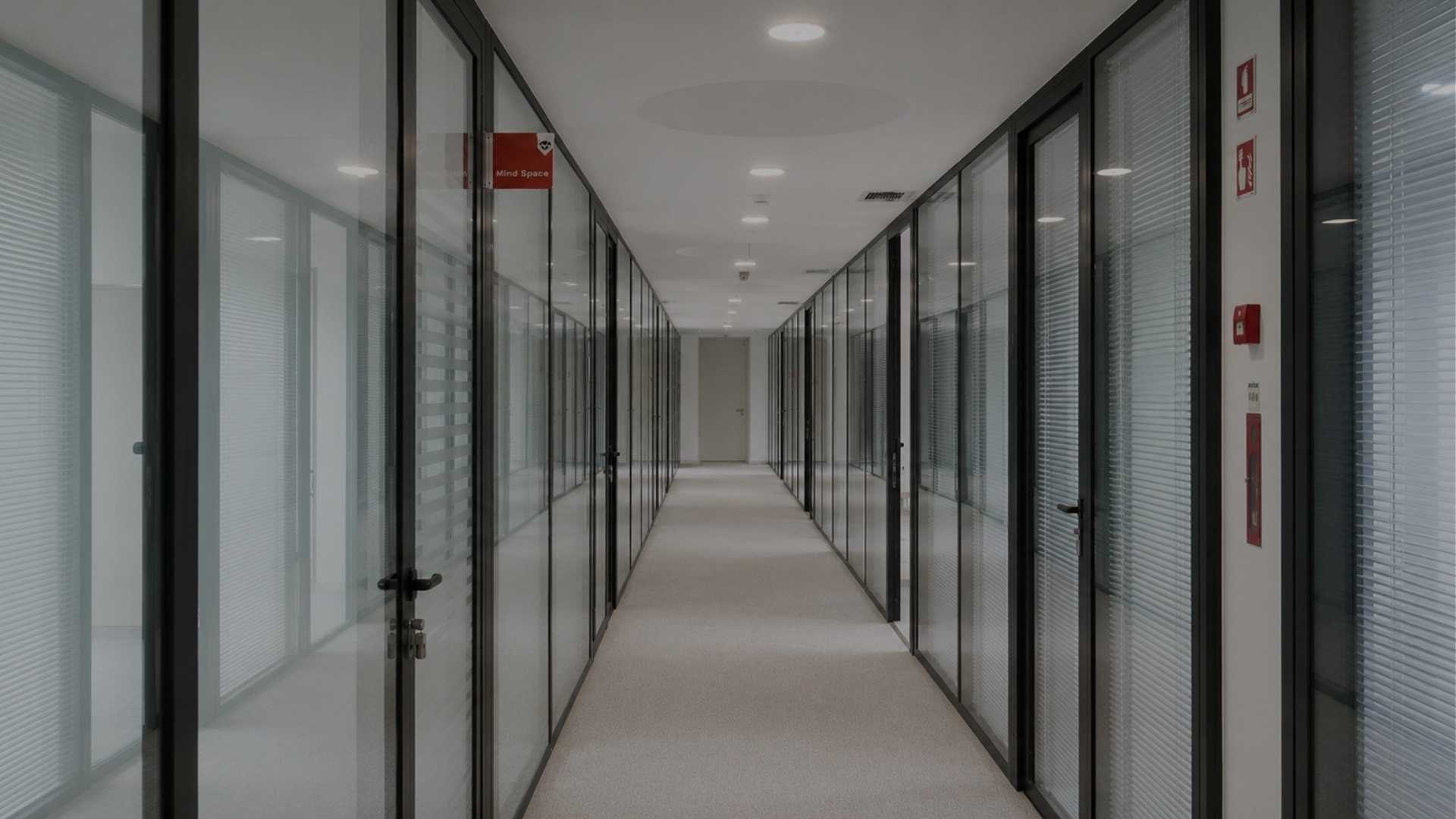 Corredor principal da MaiSpace, ladeado por gabinetes privados com divisórias em vidro, portas de acesso em alumínio e iluminação embutida no teto.