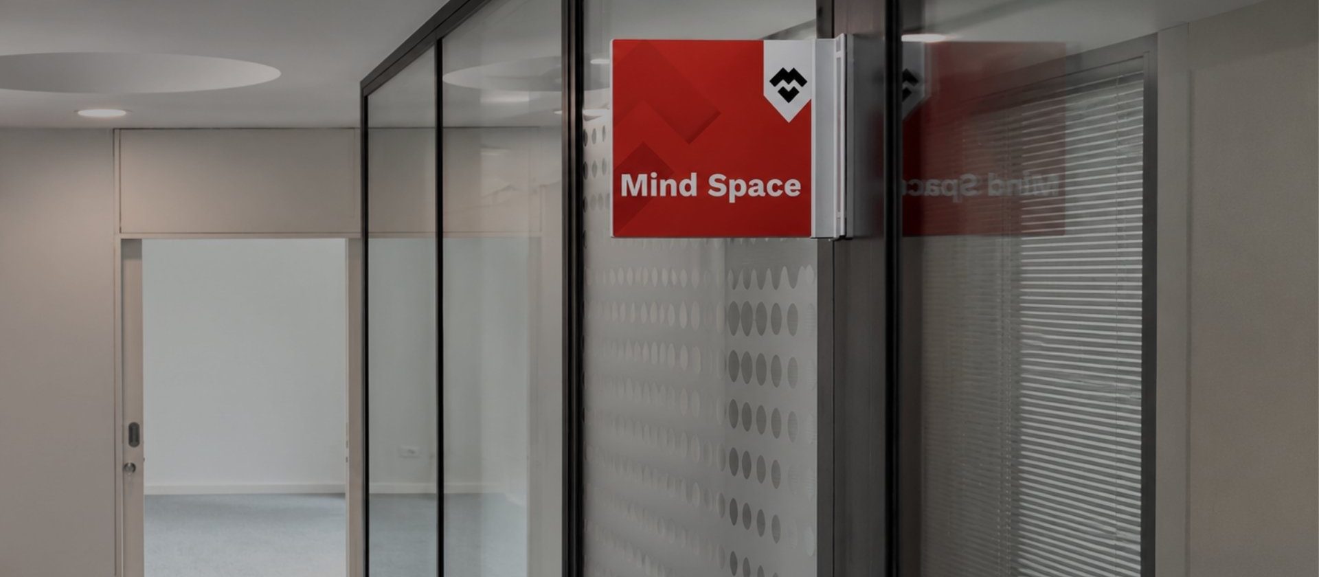 Entrada da sala Mind Space na MaiSpace, com sinalética identificativa e divisórias em vidro.