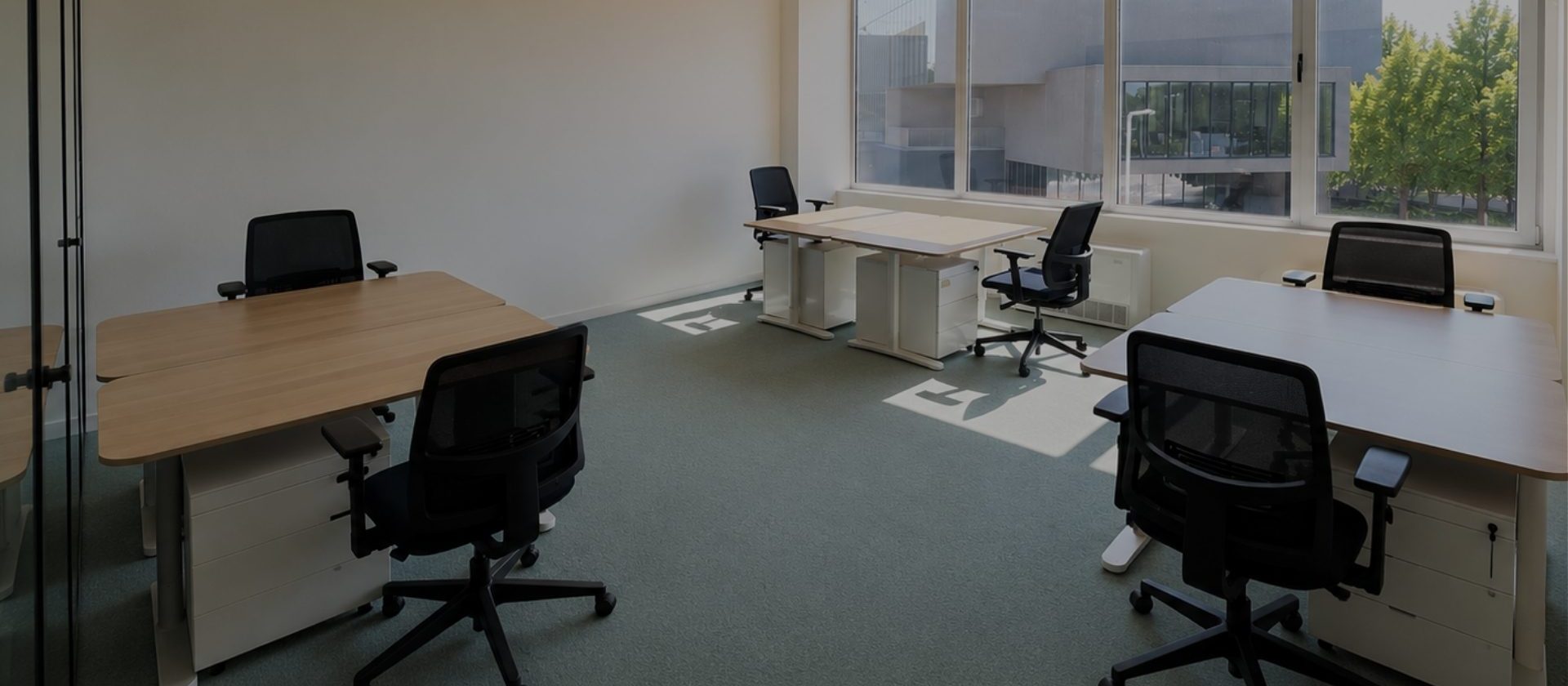 Escritório privado da MaiSpace com secretárias de madeira, cadeiras ergonómicas pretas, janela ampla com luz natural e vista para o exterior.