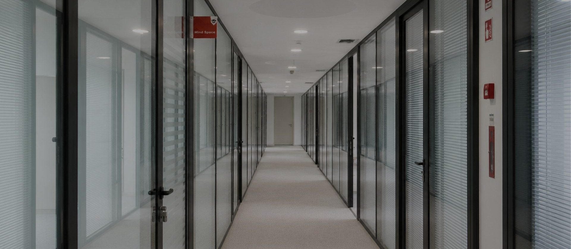 Corredor principal da MaiSpace, ladeado por gabinetes privados com divisórias em vidro, portas de acesso em alumínio e iluminação embutida no teto.